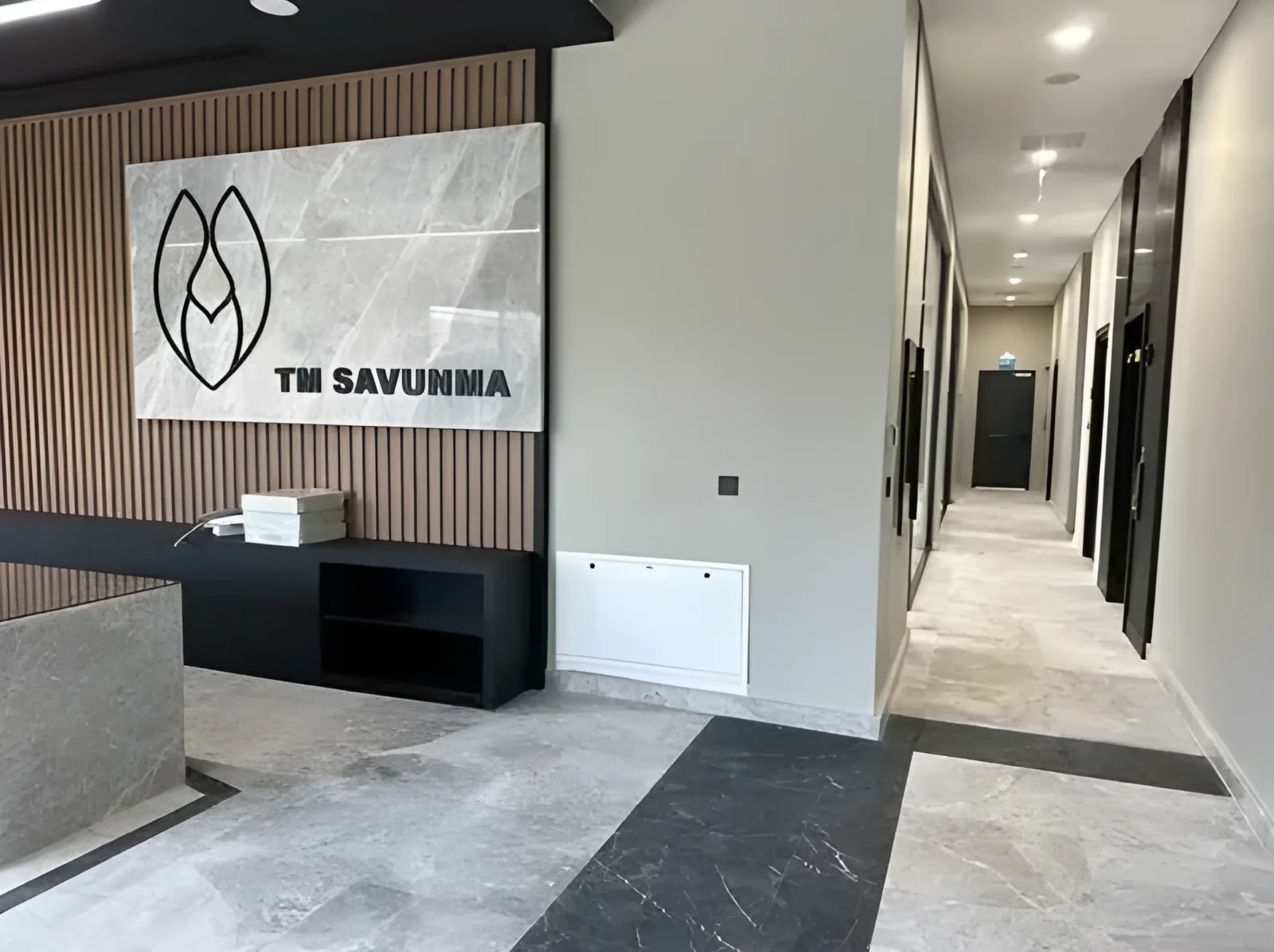 Ahşap lambri duvar ve mermer TM Savunma logo paneliyle resepsiyon ve koridor