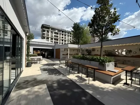 Ağaçlar arasında uzanan oturma bankları ve kafe yapıları